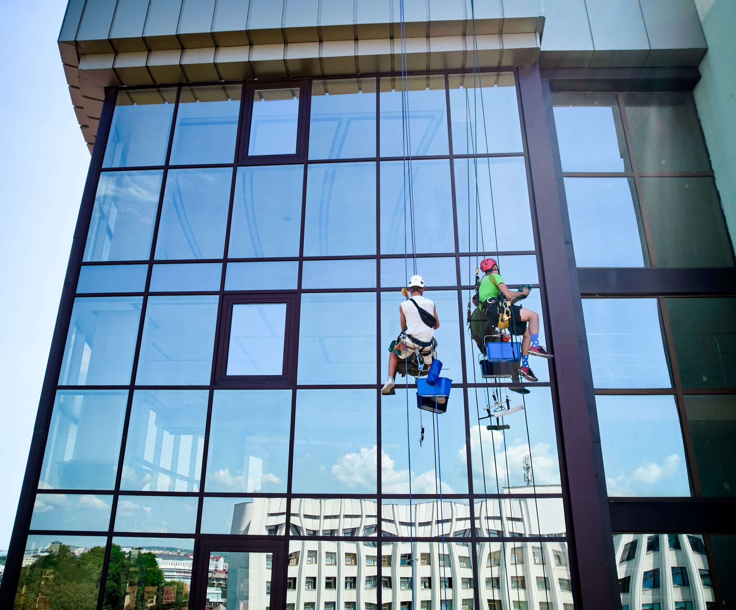 Industrial mountaineering worker cleaning window outside building.